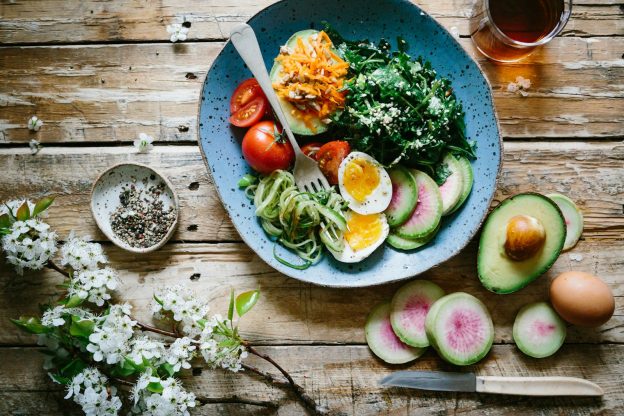 A bowl of vegetables, egg and avocado on a wooden table